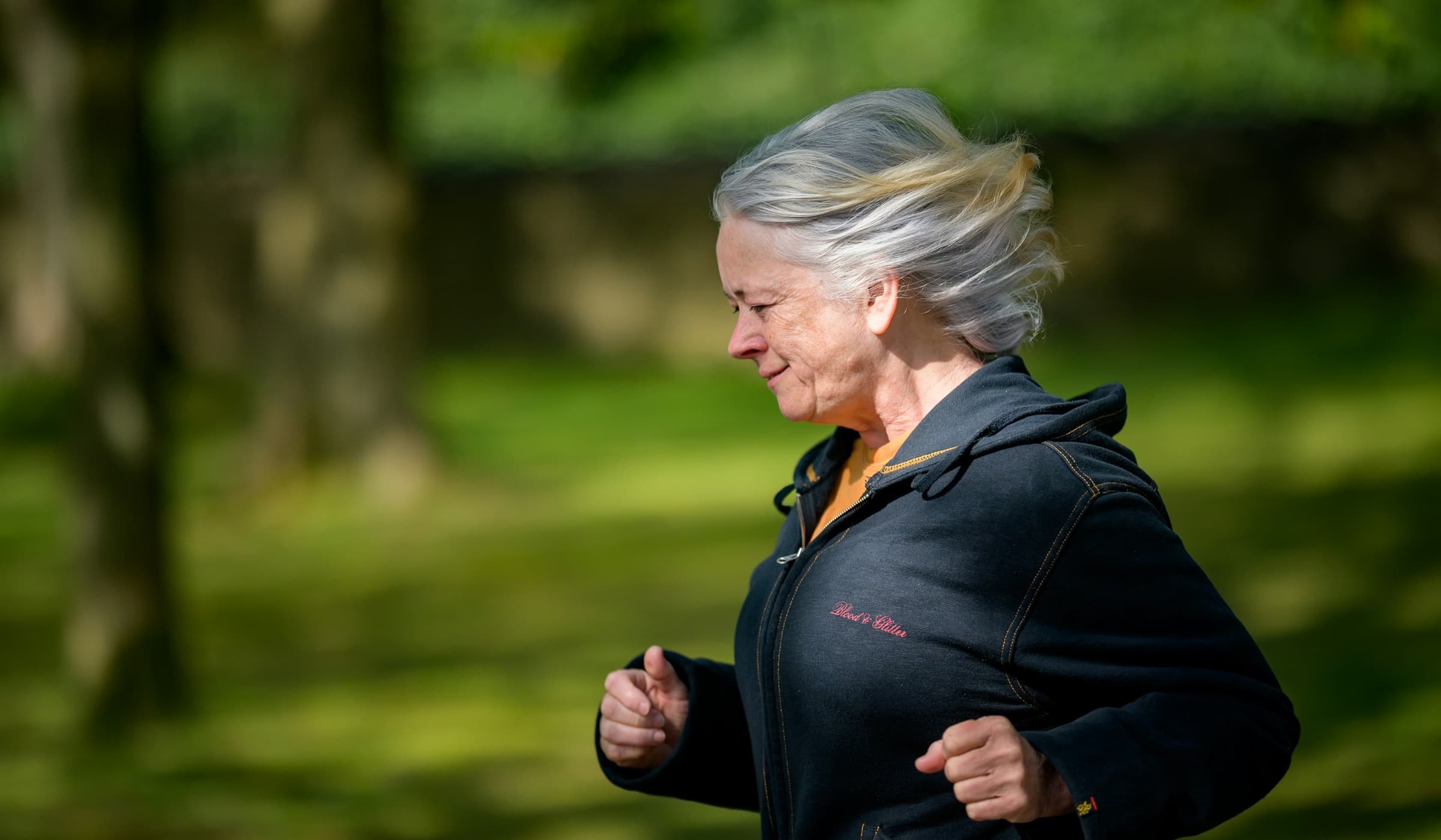 A woman with silver hair running through a park