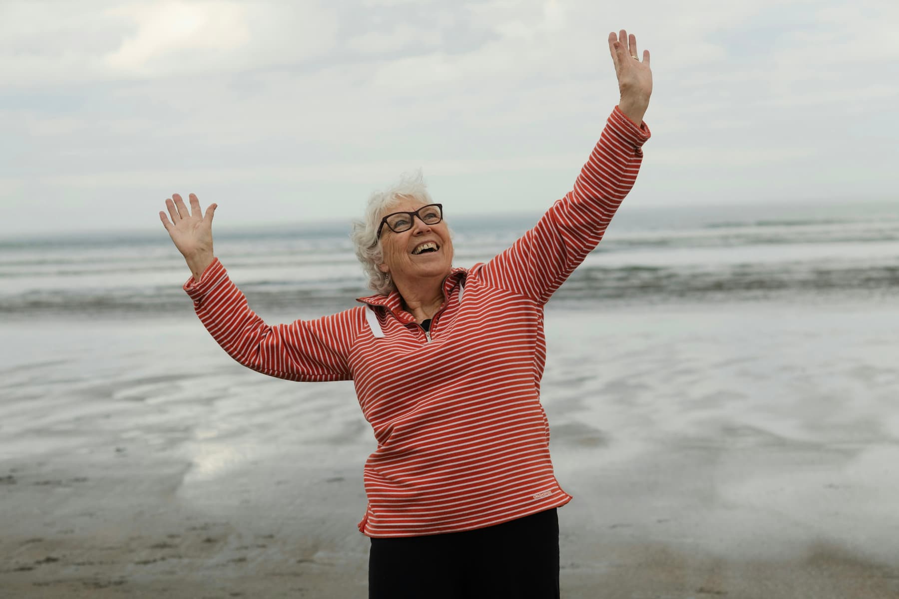 An older woman with her arms raised on a beach