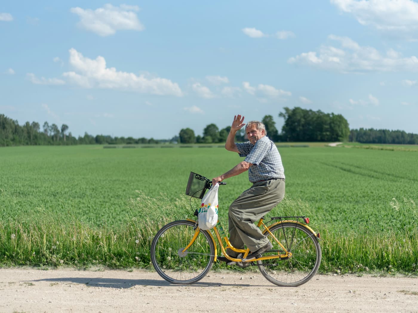 An older man riding a bicycle on a country road, waving