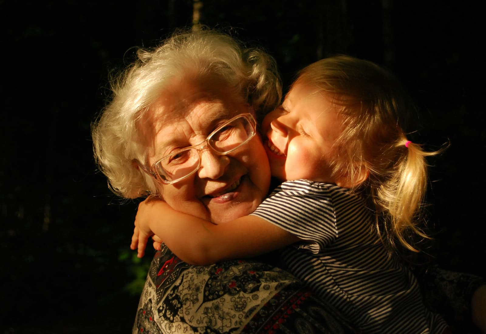 A grandmother laughing while her granddaughter hugs her