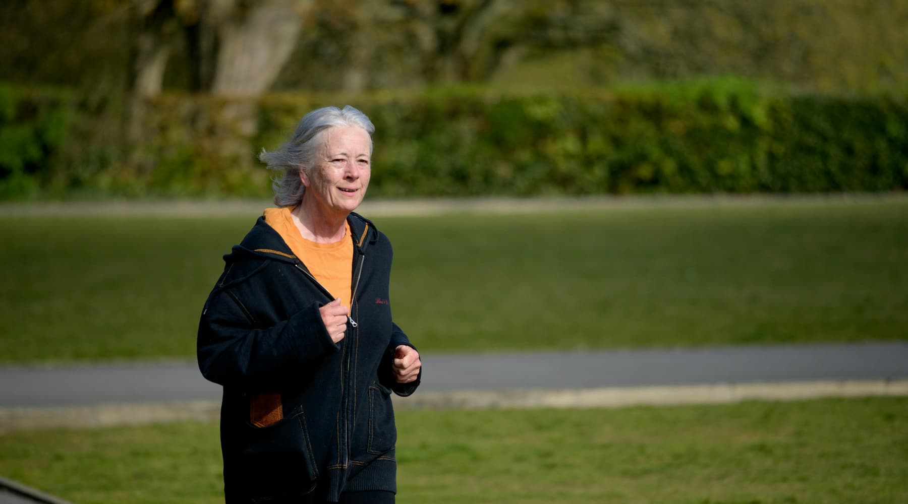 A woman with silver hair jogging along a park path